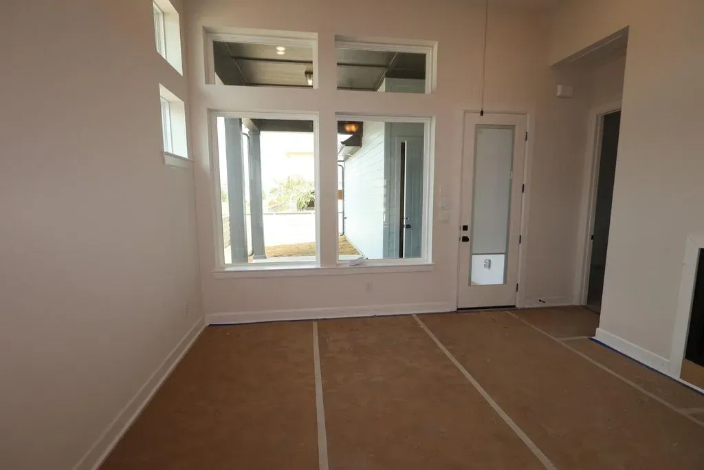 Empty new-construction living room before AI virtual staging, with bare walls, transom windows, a glazed side door, an unfinished fireplace surround and brown protective floor covering taped to the subfloor