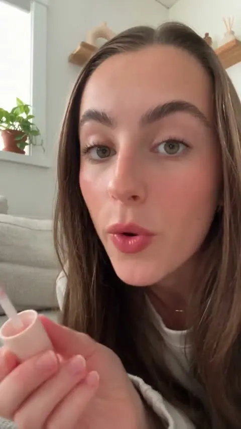 AI UGC ad: a creator on a sofa applying a pink lip oil while talking to camera